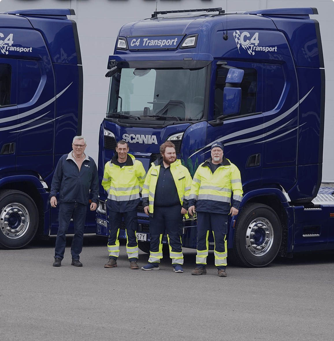 Fyra m&auml;n st&aring;r framf&ouml;r tv&aring; bl&aring; C4 Transport-lastbilar, tre if&ouml;rda gula s&auml;kerhetsuniformer.