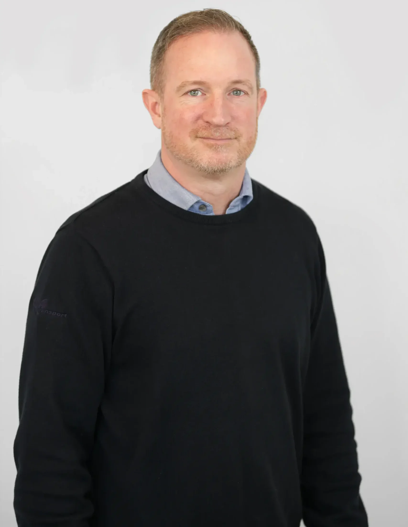 Man med kort hår och skägg klädd i en svart tröja, stående mot en ljus bakgrund.