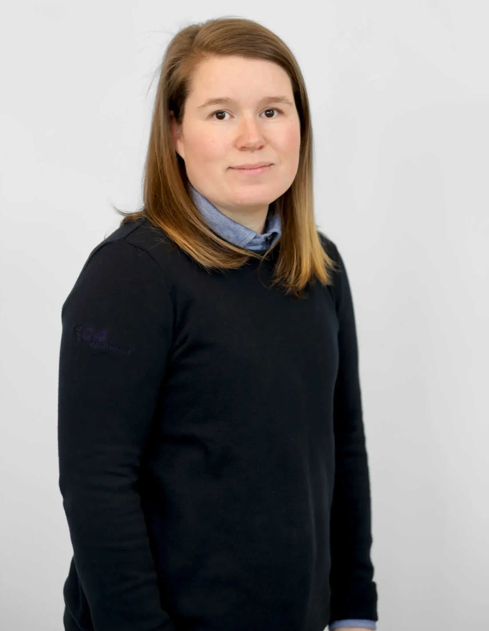 En kvinna med rakt brunt hår i en svart tröja står mot en vanlig vit bakgrund.