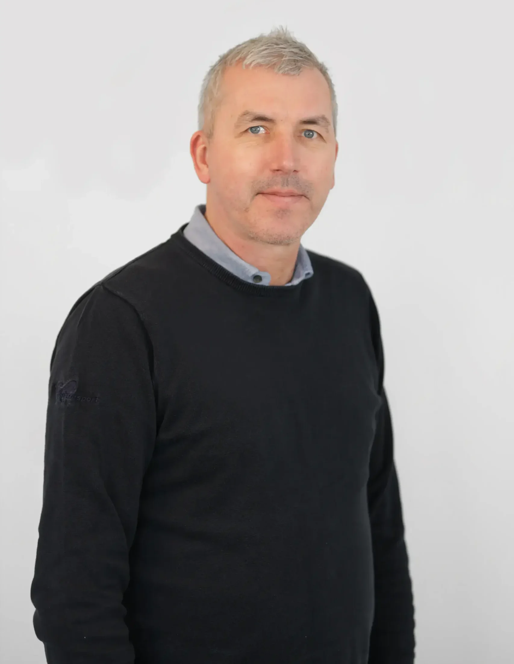 En medelålders man med kort grått hår iklädd en svart tröja står mot en vit bakgrund.