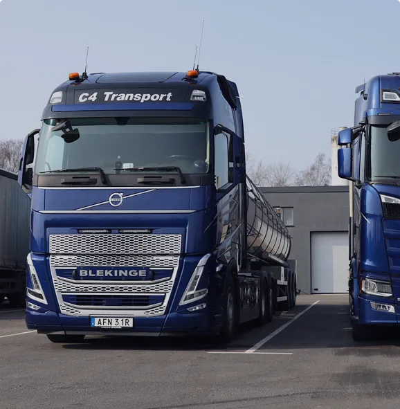 Blå Volvo tankbil märkt C4 Transport parkerad på en tomt bredvid en annan lastbil.